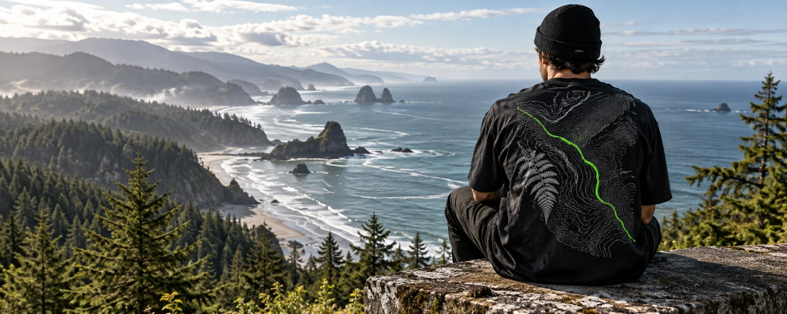 Campaign concept: black graphic tee overlooking a forest coastline